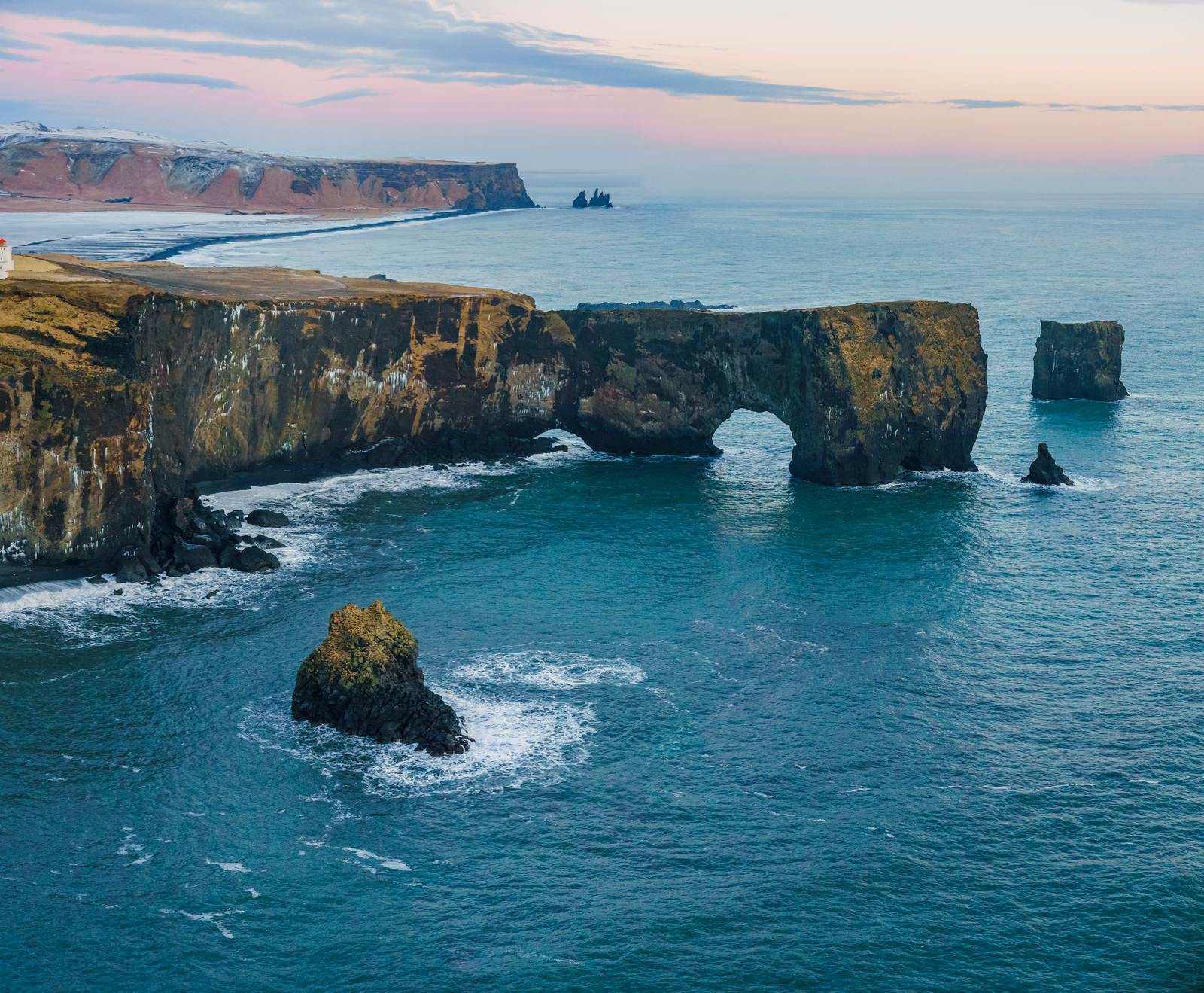 Dyrhólaey sea arch and cliffs above the South Coast with Reynisdrangar visible in the distance.