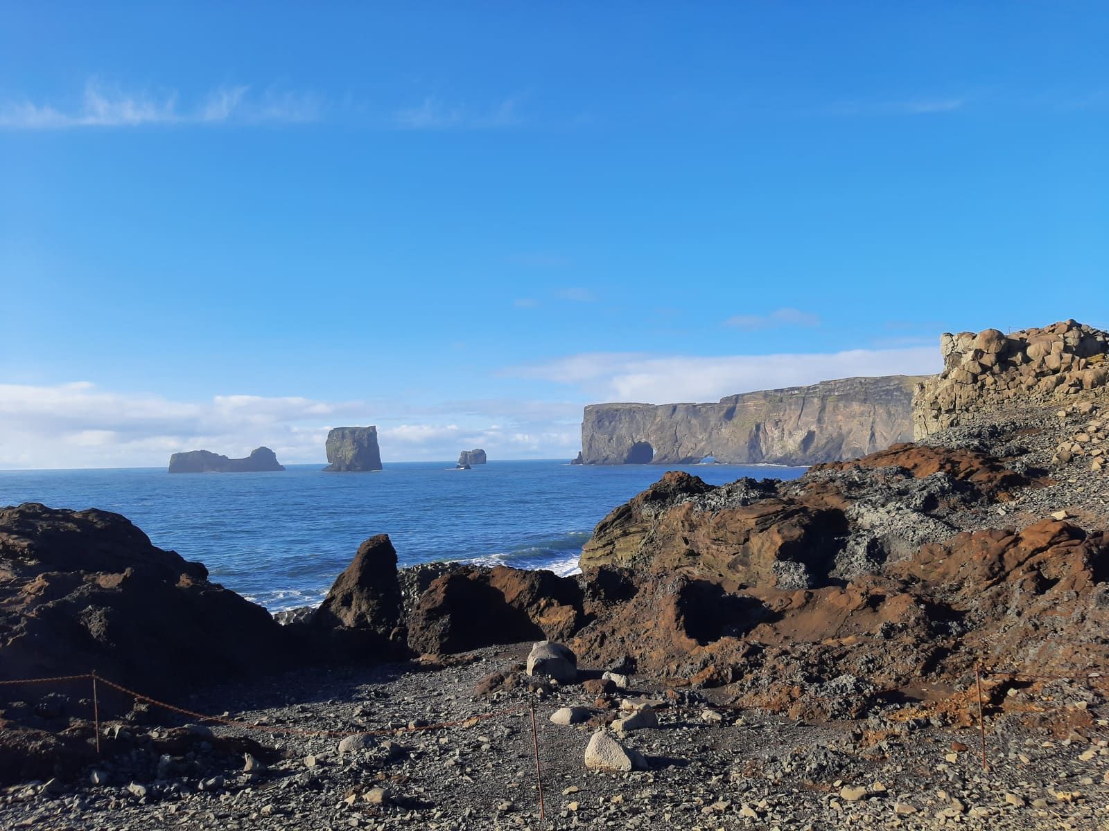Rocky foreground at Dyrhólaey with cliffs and sea stacks across the water.