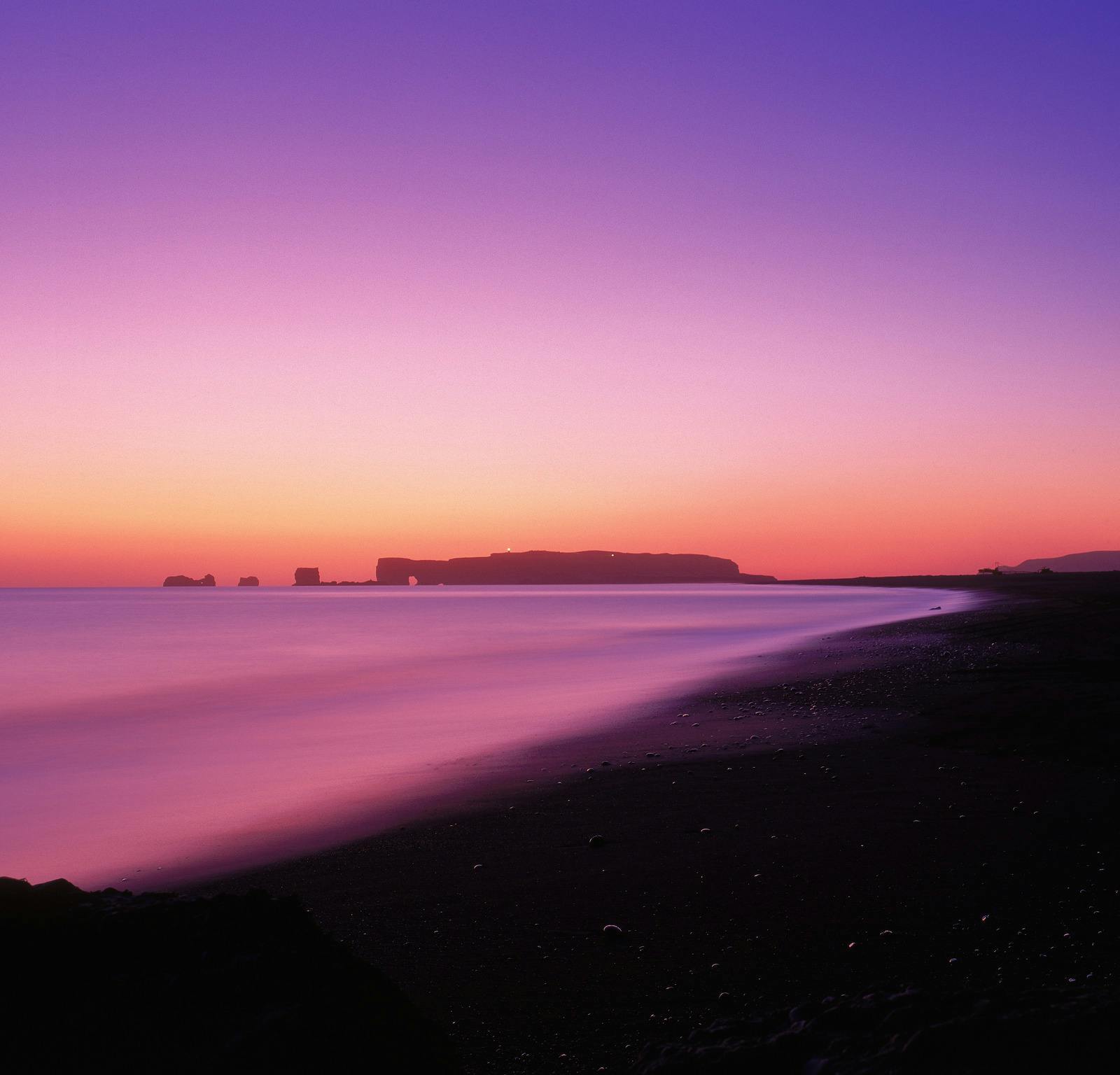 Dyrhólaey headland silhouetted beyond a black-sand beach at sunset.