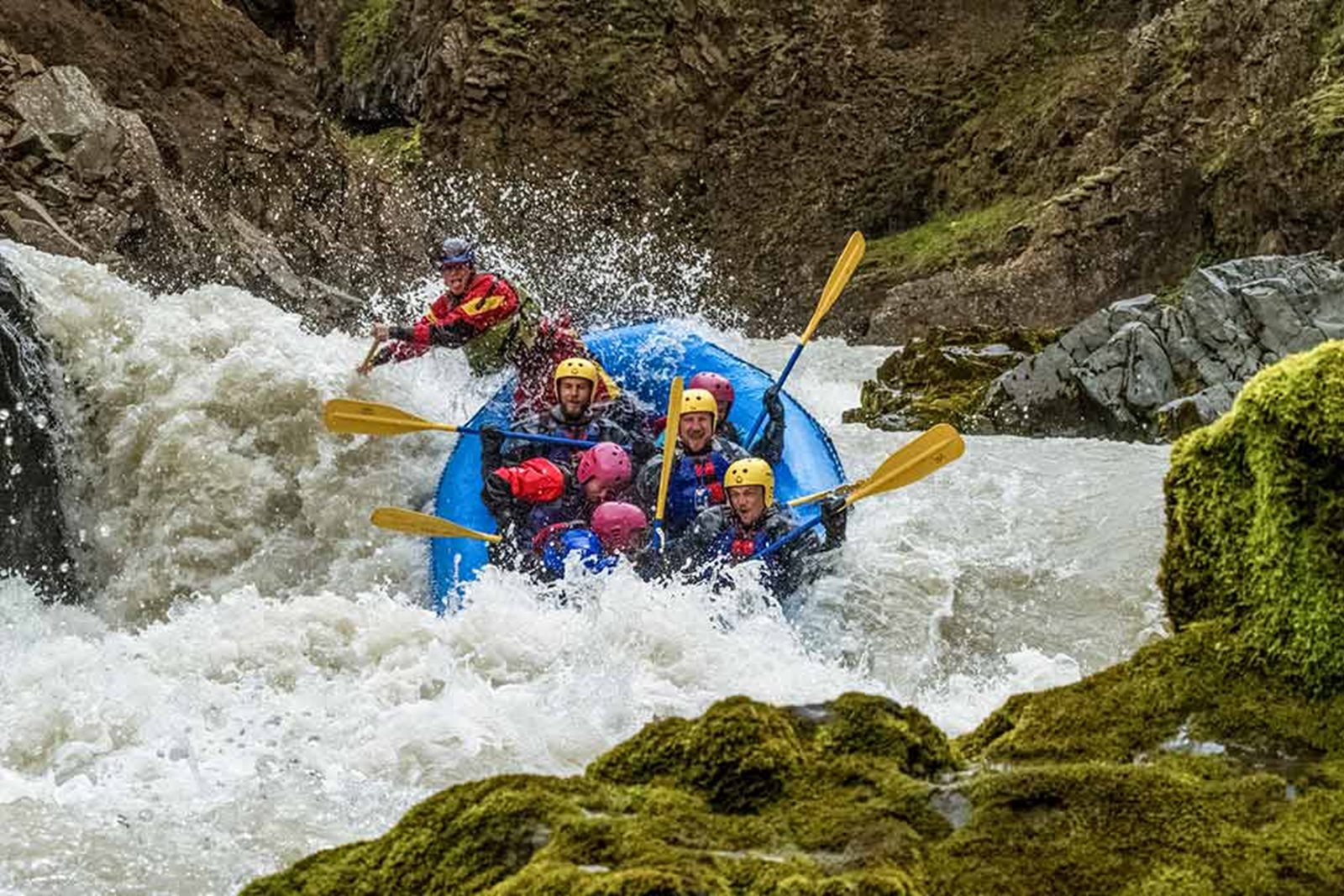 A blue rafting boat in whitewater between mossy rocks on the East Glacial River in Iceland.