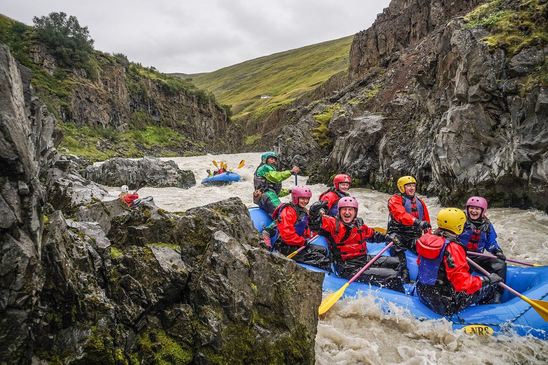 A raft descending churning water inside the Austari-Jökulsá canyon with rock walls on both sides.
