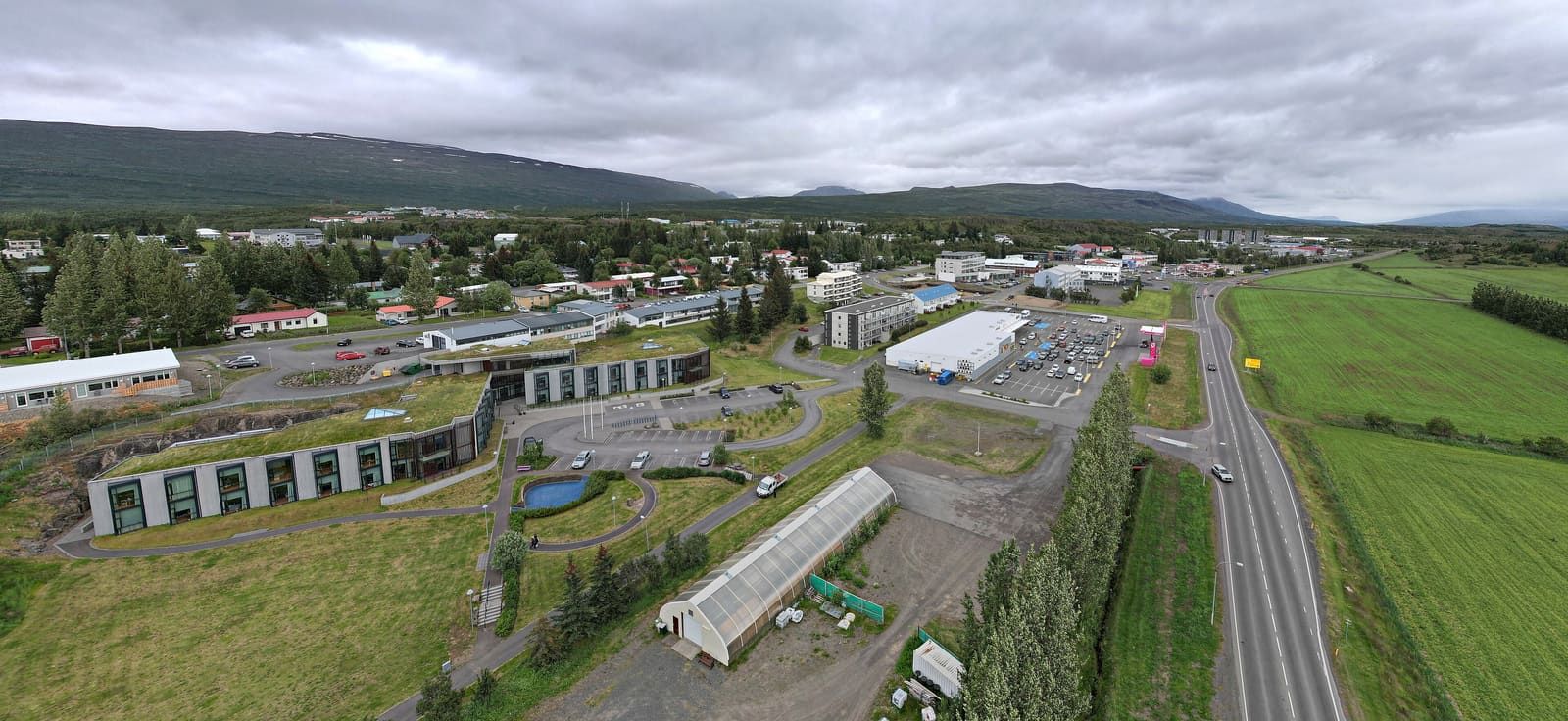 Egilsstaðir streets, houses, and service buildings below green hills and low cloud in East Iceland.