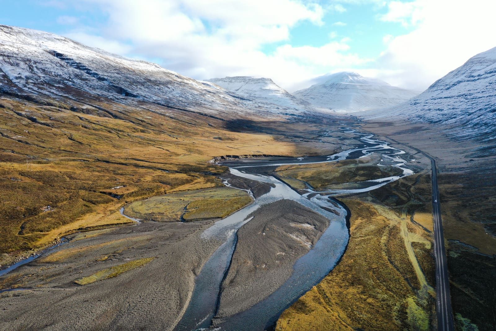 A road crossing open East Iceland valley terrain below snow-dusted mountains near Egilsstaðir.