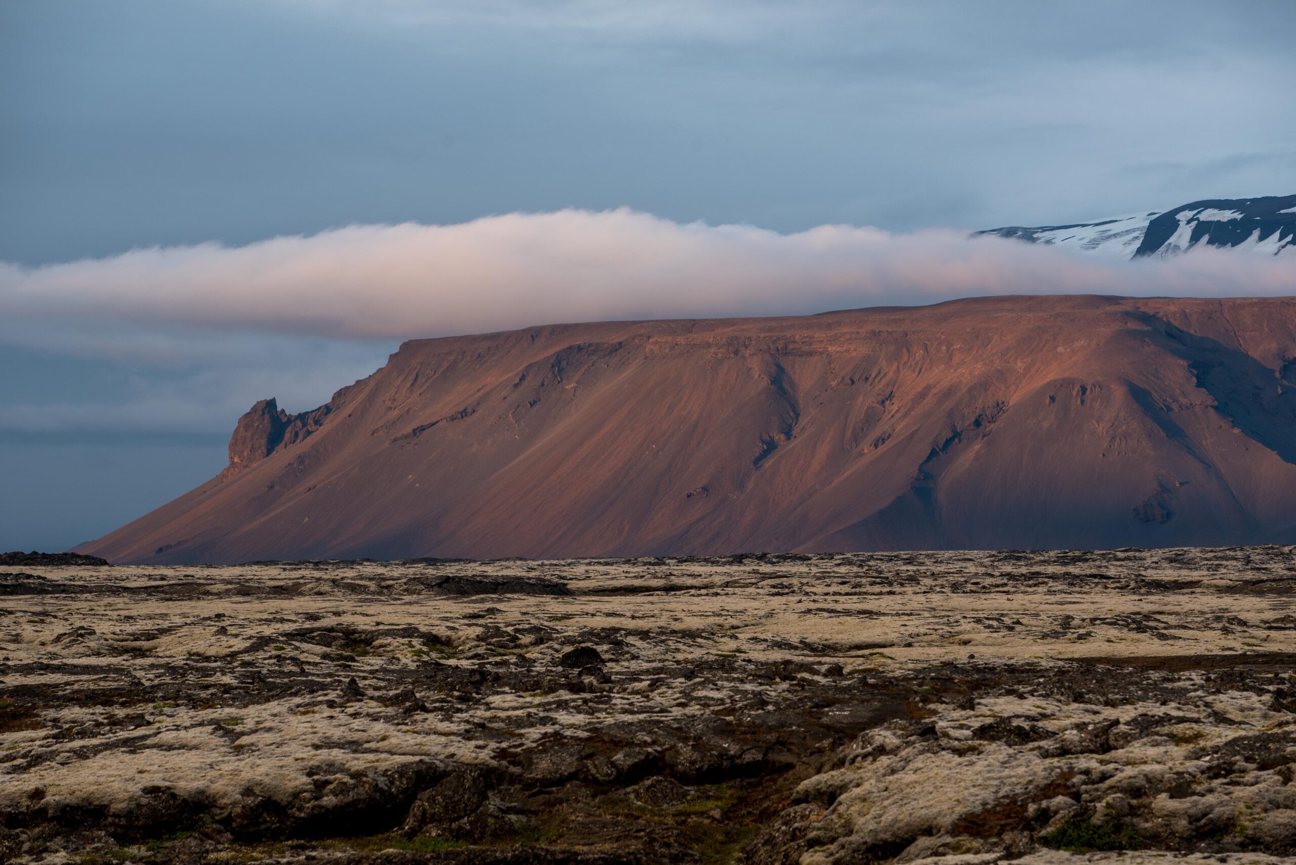 Steep brown volcanic cliffs below the snow edge of Eiríksjökull above a rough lava landscape.