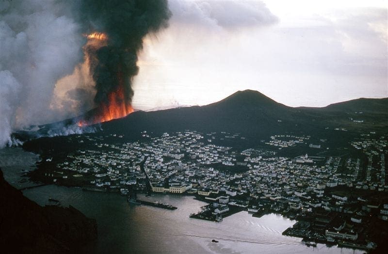 Eldfell erupting on Heimaey in 1973 with lava fountains, smoke, and the town below.