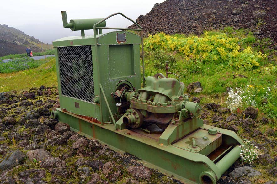 A lava-cooling pump displayed on Heimaey with Eldfell eruption history behind it.