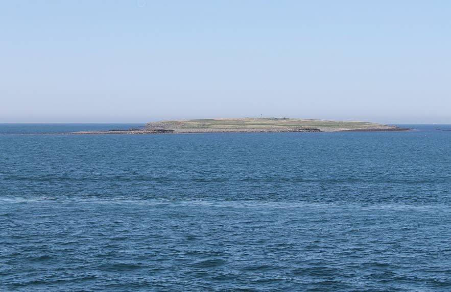 Low grassy Engey island seen across blue water in Faxaflói bay