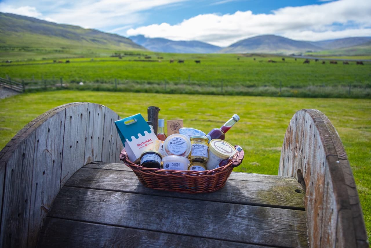 A basket of Erpsstaðir dairy products on an outdoor table above green farm fields.