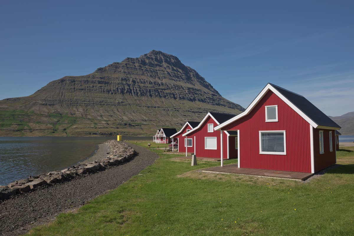Red seahouses at Mjóeyri below Hólmatindur mountain beside Eskifjörður fjord.