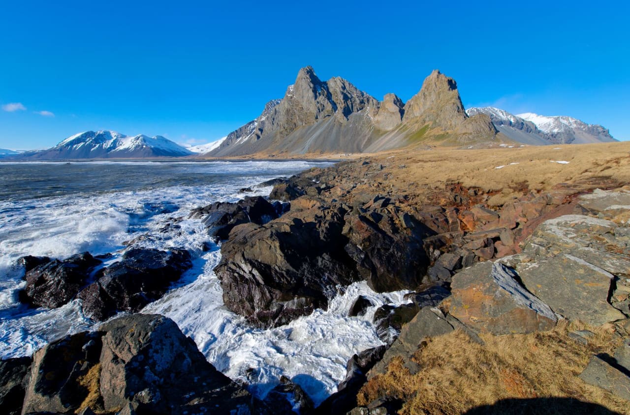 Eystrahorn rising above dark coastal rocks and surf at Hvalnes in southeast Iceland.