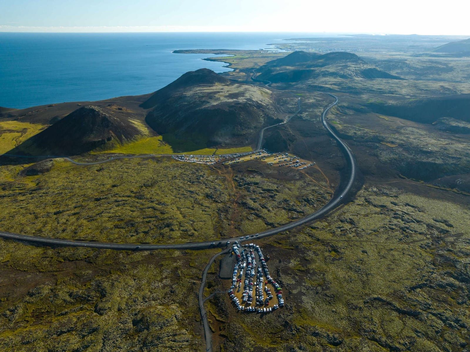 Aerial view of Fagradalsfjall parking area, access road, and surrounding crater slopes near the Reykjanes coast.