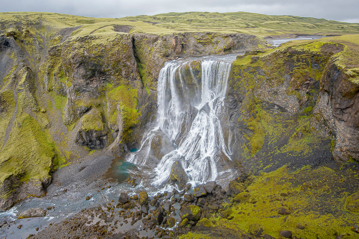 Wide view of Fagrifoss falling through a green and black canyon in the Icelandic Highlands.