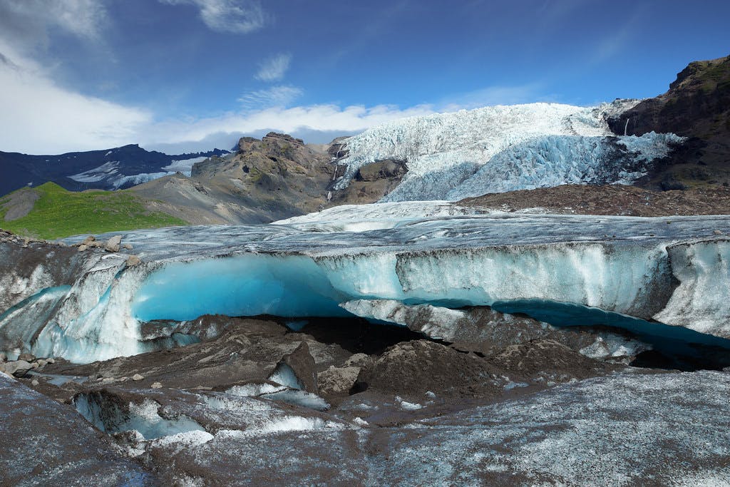 Blue ice and dark volcanic slopes on Falljökull Glacier under broken cloud.