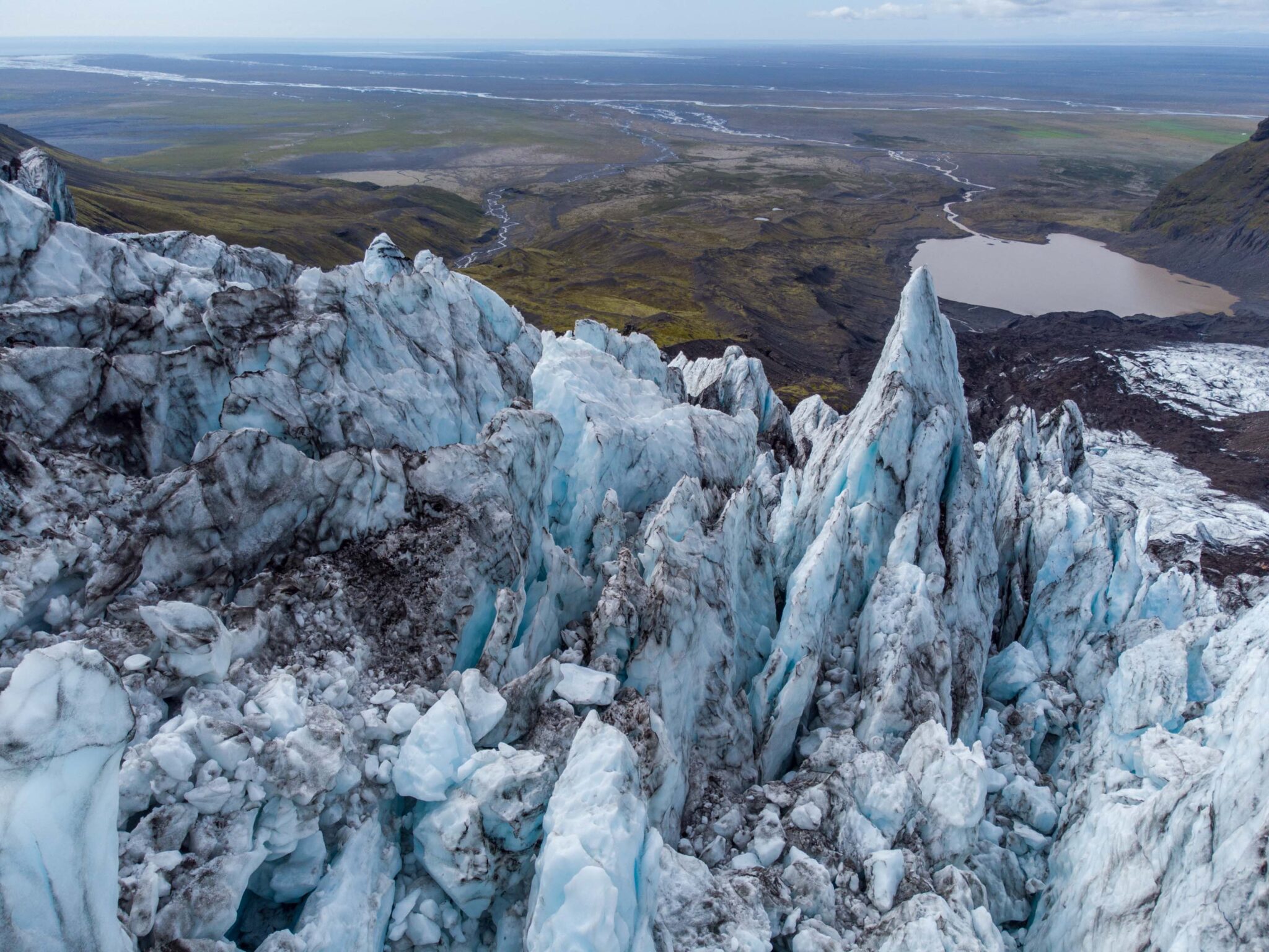 Wide valley approach below Falljökull with glacier ice, dark slopes, and rough foreground terrain.