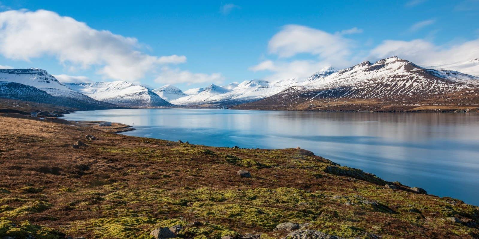 Wide view over Fáskrúðsfjörður fjord with steep green mountains and village shoreline in East Iceland.