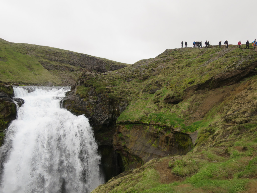 Hikers above a Skógá waterfall on the green lower section of the Fimmvörðuháls trail.