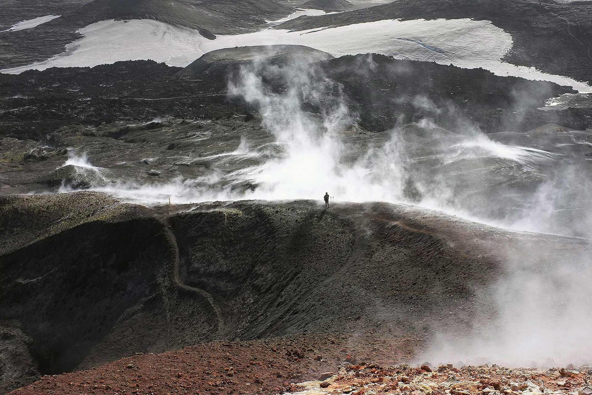 A lone hiker on the steaming volcanic pass of Fimmvörðuháls between snowy glacier edges.