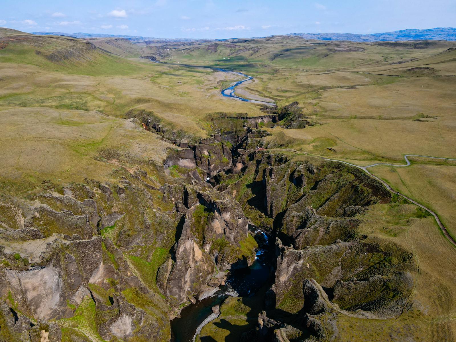 Aerial view over Fjaðrárgljúfur Canyon, with the Fjaðrá river winding through mossy South Iceland cliffs.