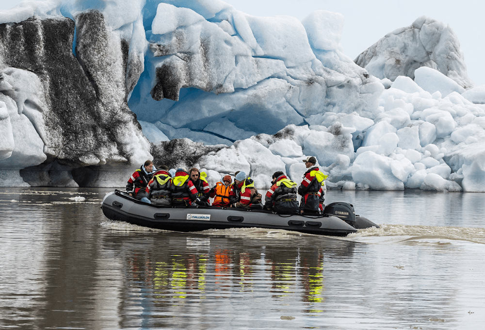 A Fjallsárlón boat moving between large blue-white icebergs on the glacier lagoon.