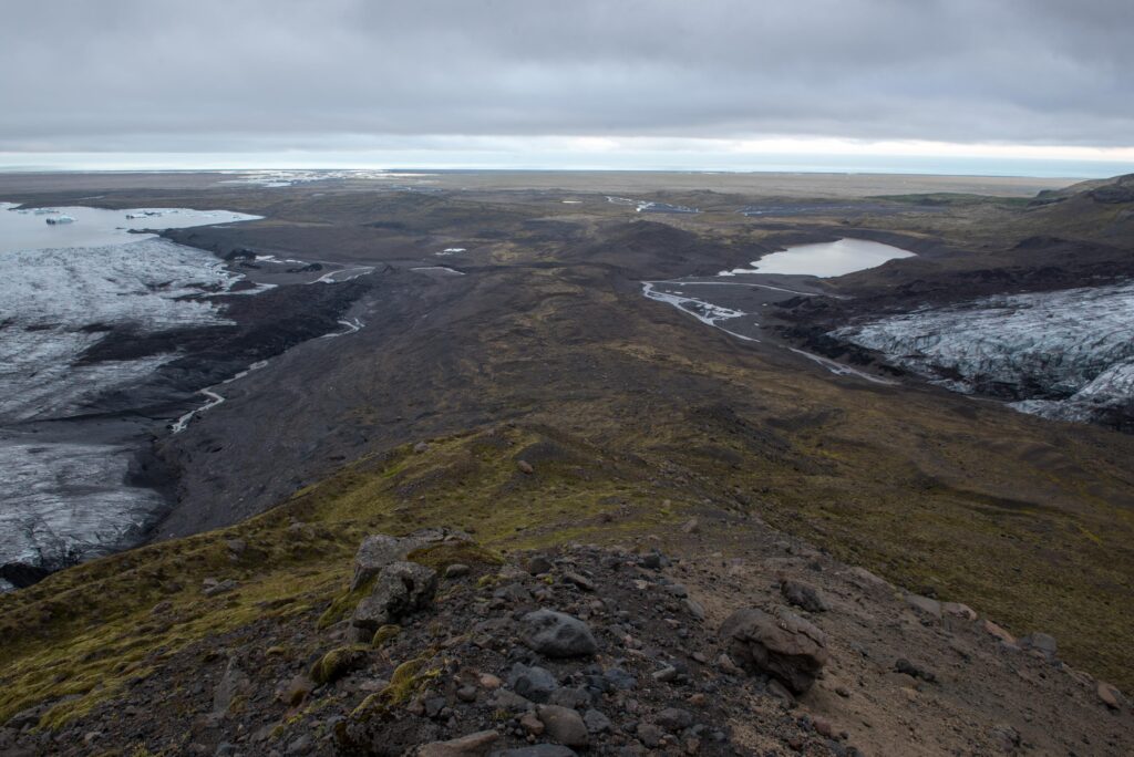 A rocky ridge between glacier tongues near Fjallsjökull with lowland water and the coast beyond.