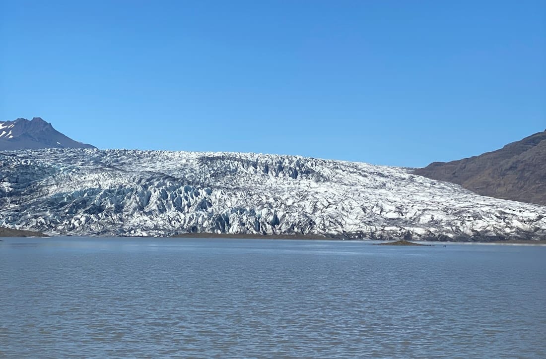 Blue-white front of Fláajökull glacier across a calm glacial lagoon.
