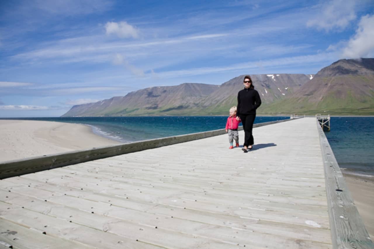 Wooden pier and pale Holtsfjara beach across Önundarfjörður from Flateyri with mountains beyond.