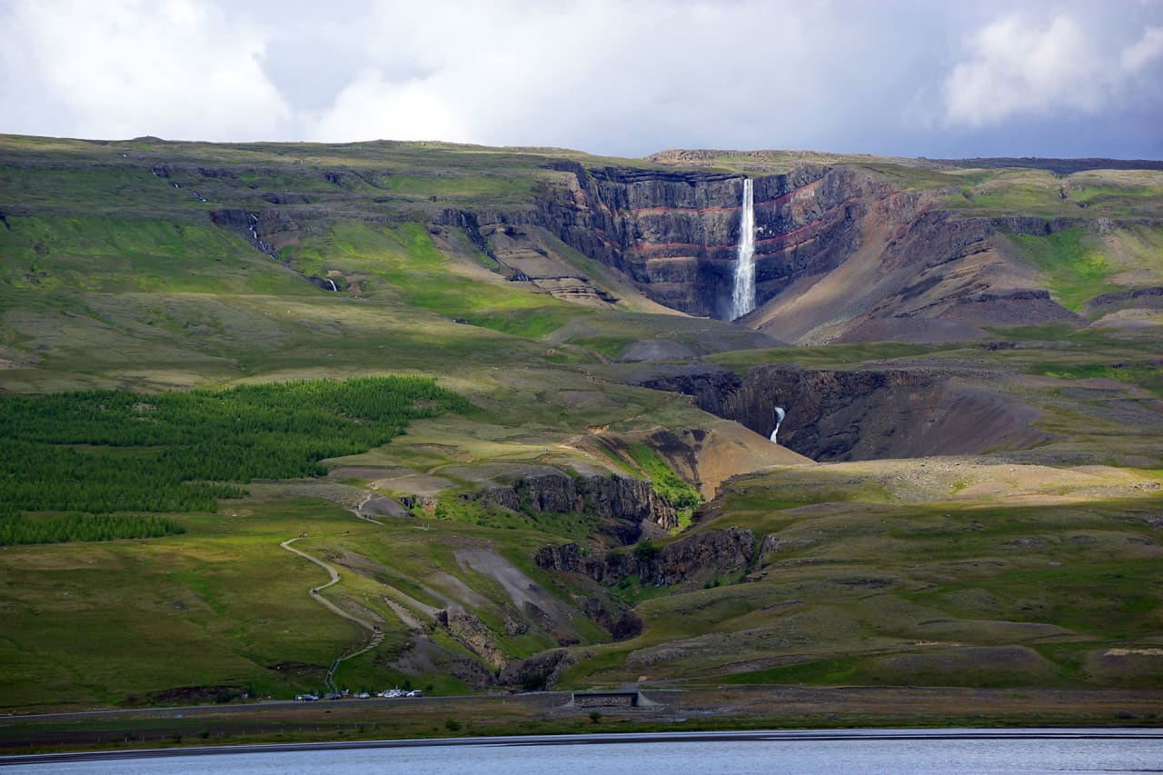 Hengifoss waterfall across Fljótsdalur with Lagarfljót and green slopes below the red-striped gorge.