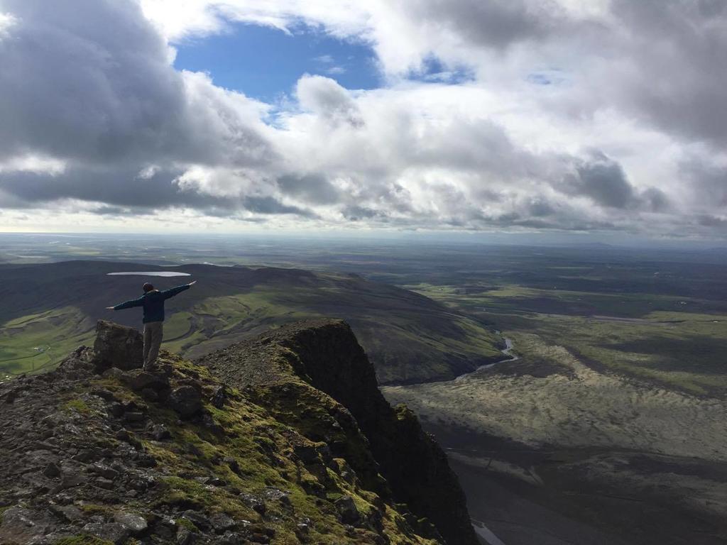 A hiker standing above the Fljótshlíð countryside with broad South Iceland views below.