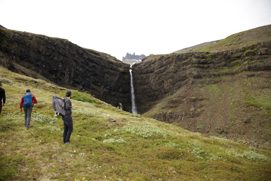Hikers below Flögufoss as the waterfall drops through the Breiðdalur gorge in East Iceland.