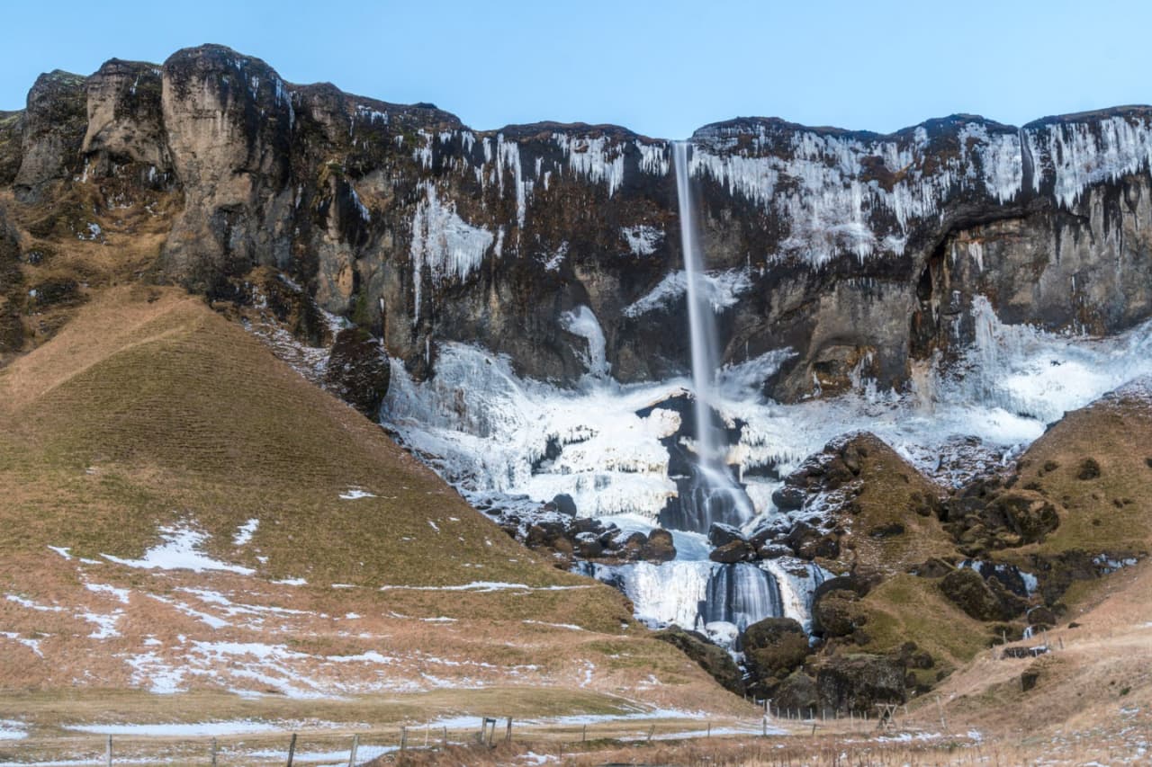 Foss á Síðu dropping from a dark cliff with snow patches around the cascade.