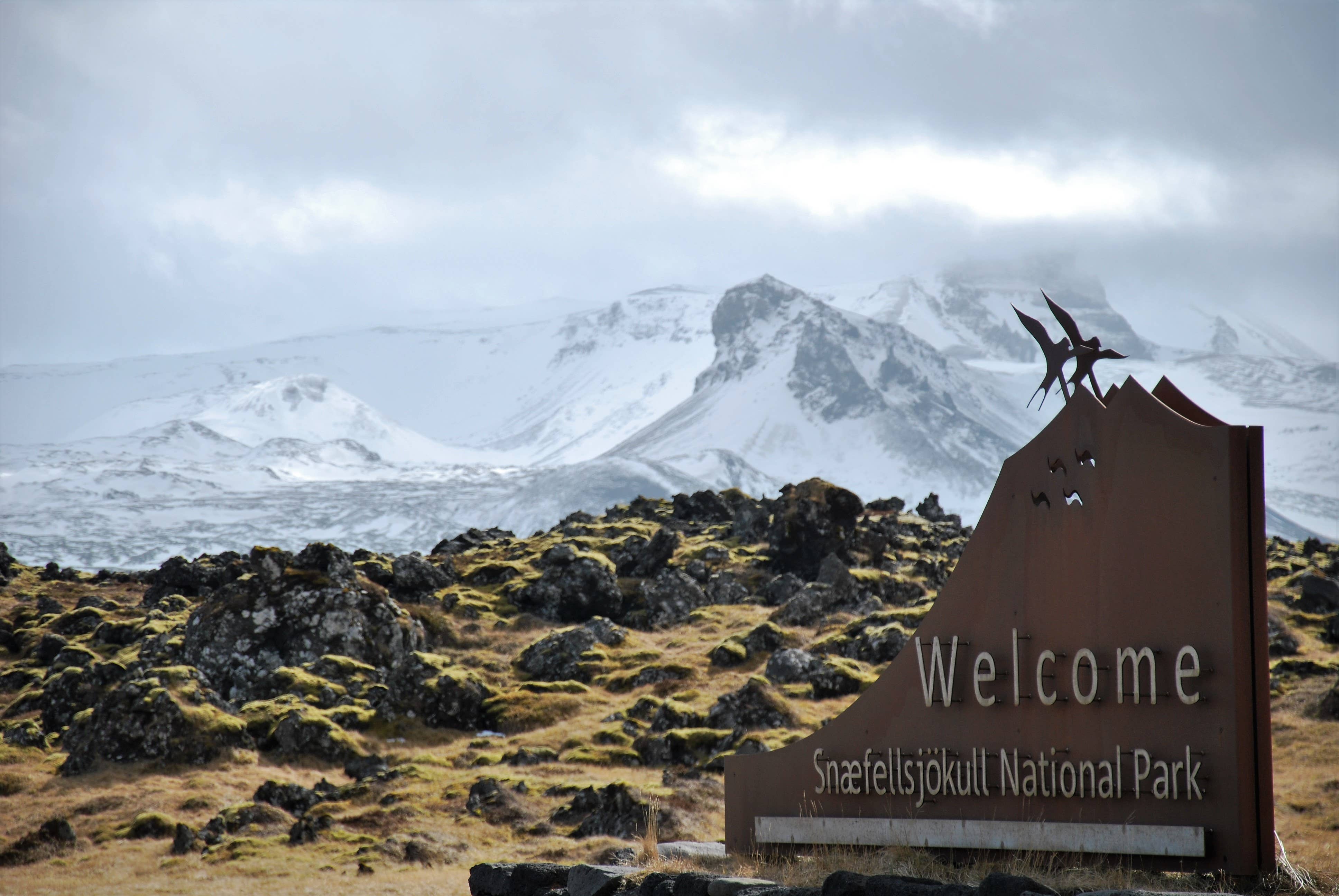 Snæfellsjökull National Park sign near Arnarstapi with snowy mountains behind it.