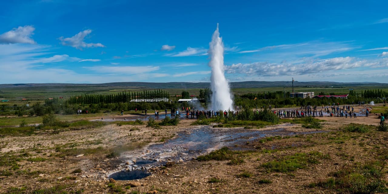 Strokkur erupting in the Geysir geothermal area with visitors watching from marked paths.
