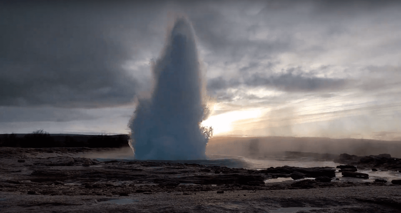 A tall Strokkur eruption rising from the Geysir geothermal area under cloudy light.