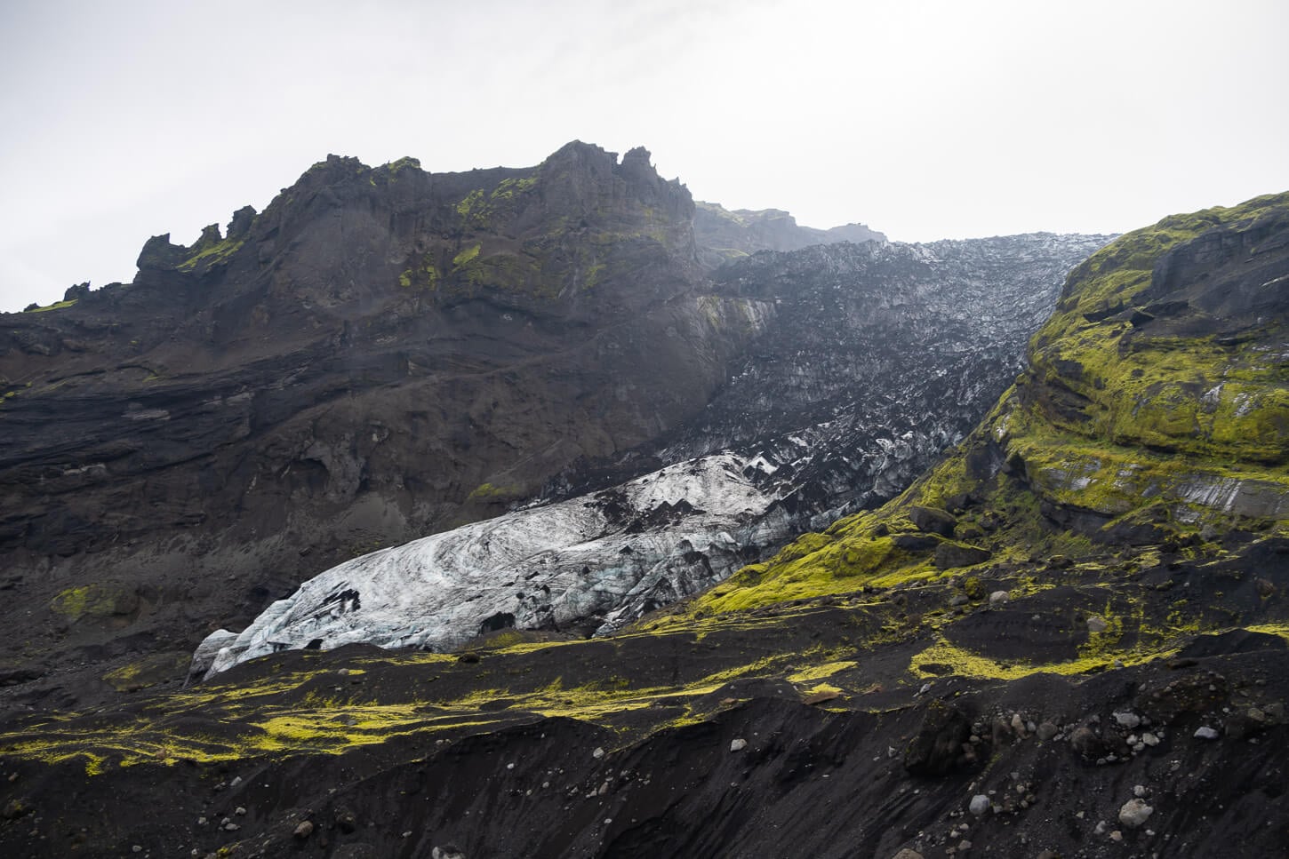 Ash-darkened ice and mossy volcanic slopes around Gígjökull in cloudy weather.