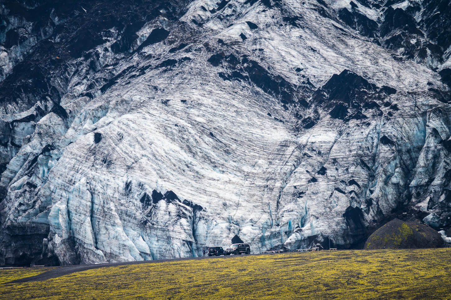 Vehicles dwarfed by the steep ice face of Gígjökull outlet glacier.