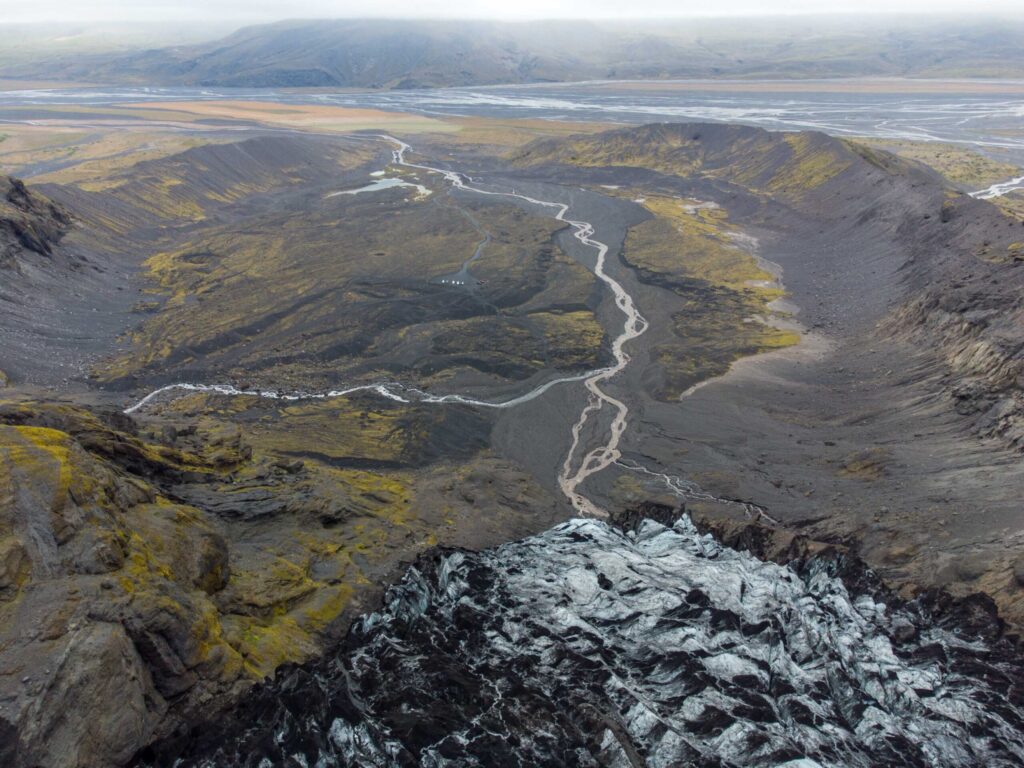 The moraine basin below Gígjökull with braided meltwater channels and dark volcanic ridges.