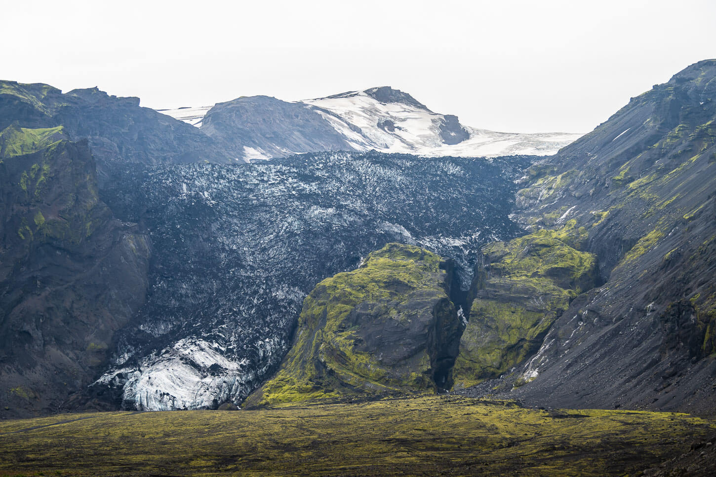 Gígjökull seen across a mossy valley with the glacier descending between dark ridges.