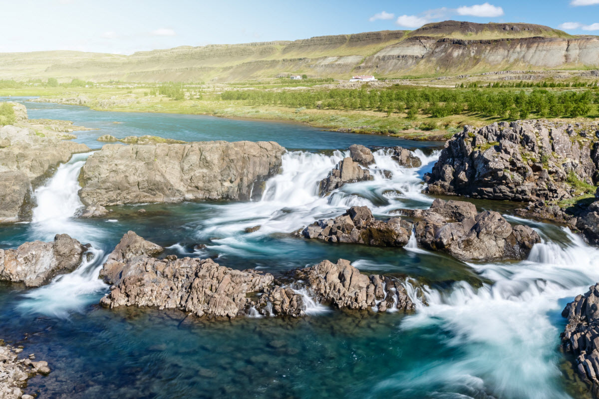Glanni Waterfall splitting into several channels across dark rock with hills behind it.