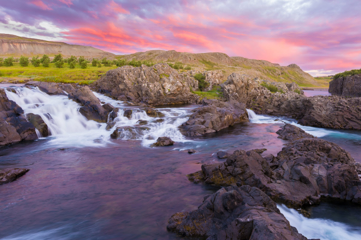 Glanni Waterfall and lava rock under colorful evening clouds.