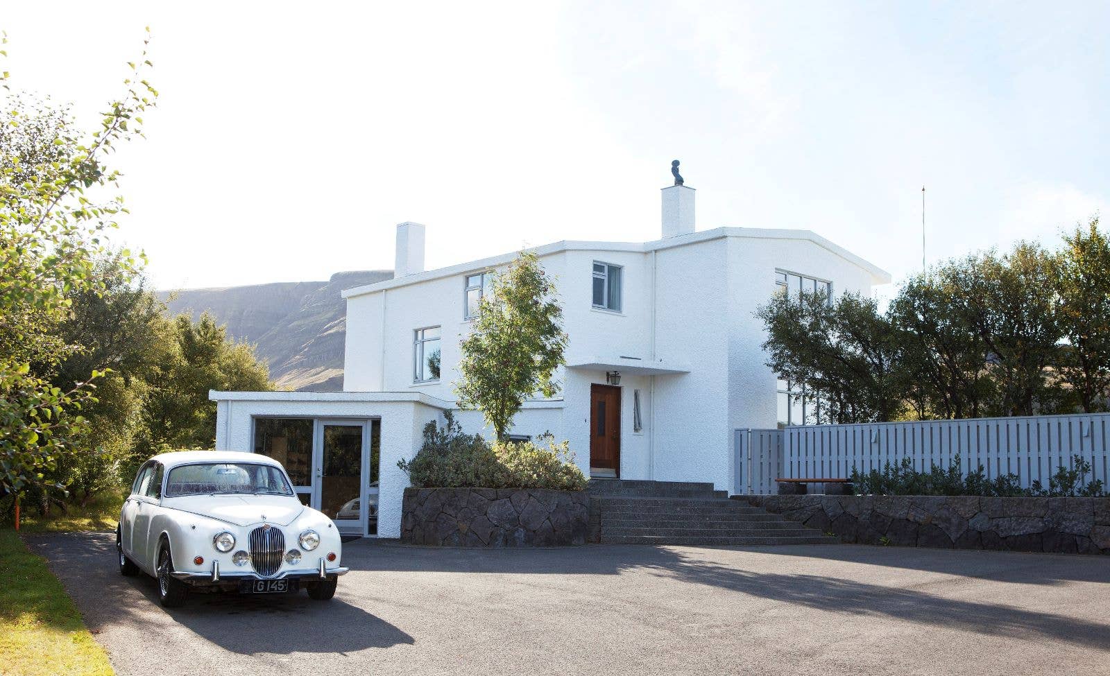 The white Gljúfrasteinn house museum in Mosfellsdalur with a vintage car outside.