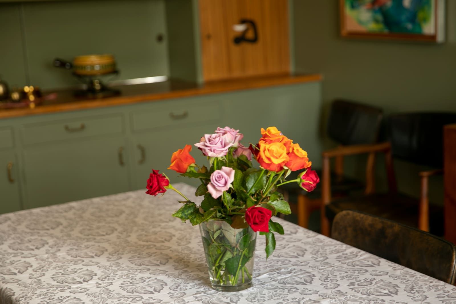A vase of roses on a table inside Gljúfrasteinn with the preserved room softly visible behind it.