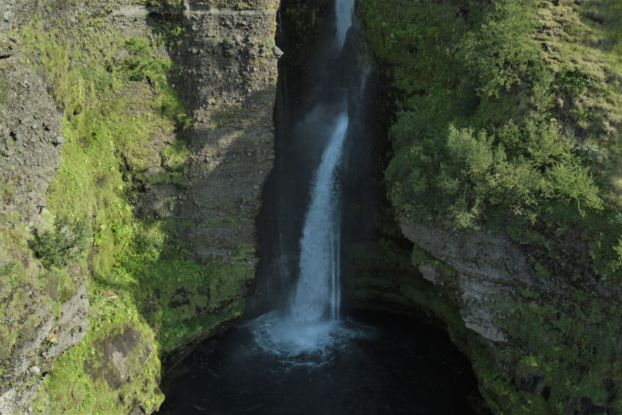 Close view of Gluggafoss falling into a dark pool below green cliffs.