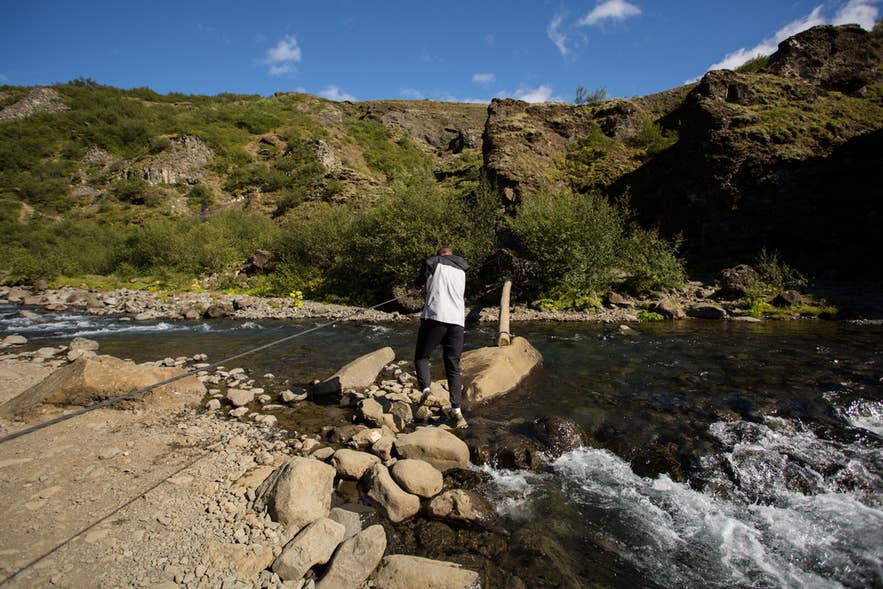 A hiker using a rope and log crossing on the Glymur trail in West Iceland.