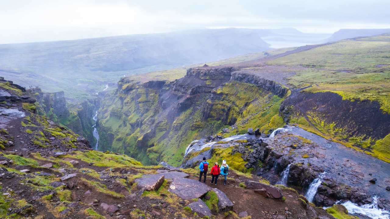 Hikers above the Glymur canyon with Hvalfjordur landscape stretching behind them.