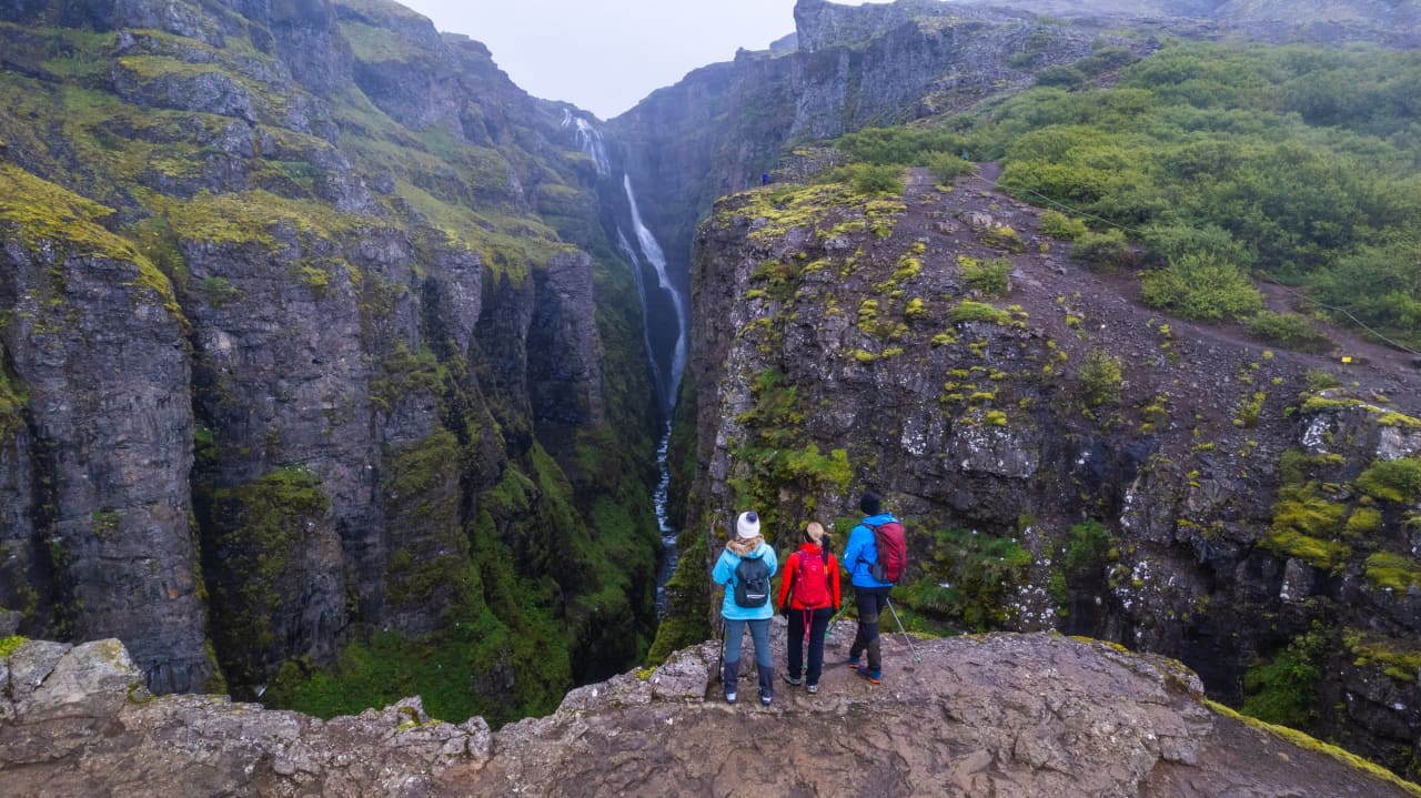 Hikers standing on the Glymur canyon trail with the waterfall dropping between steep cliffs.