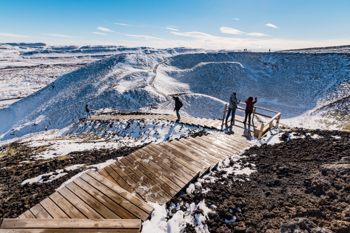 Snowy wooden steps and visitors on the rim of Grábrók crater in West Iceland.