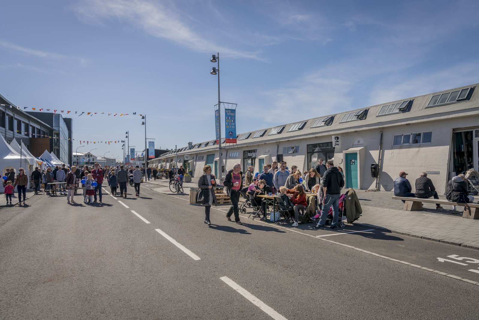 People walking through Reykjavík’s Grandi district beside low harbour buildings and cafe seating