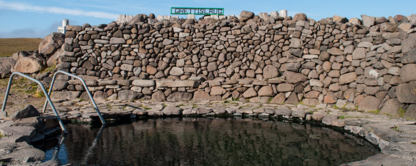Stone wall and Grettislaug sign beside the hot spring pool at Reykir on Reykjaströnd.