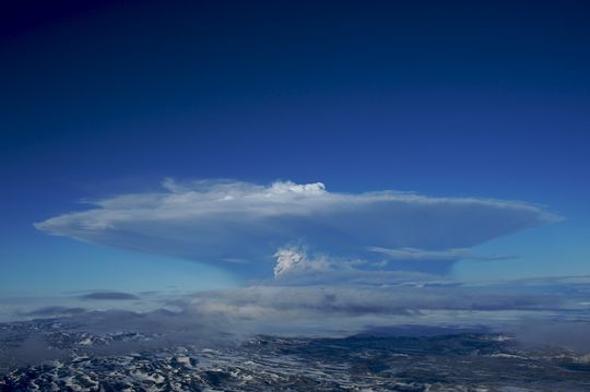 Distant Grímsvötn eruption plume rising above Vatnajökull under a blue sky.