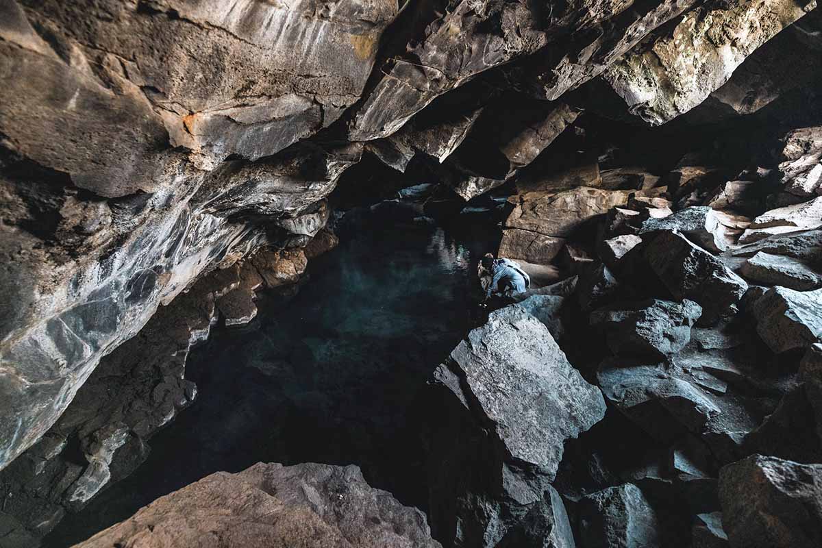 Dark lava rocks and a small pool inside Grjótagjá cave showing the uneven footing near the water.